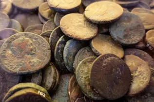A collection of old Roman coins stacked together, displaying various historical markings and patinas.