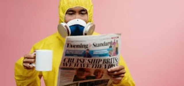 A man wearing a yellow hazmat suit is holding a newspaper, highlighting a serious approach to safety and information.