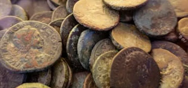 A collection of old Roman coins stacked together, displaying various historical markings and patinas.